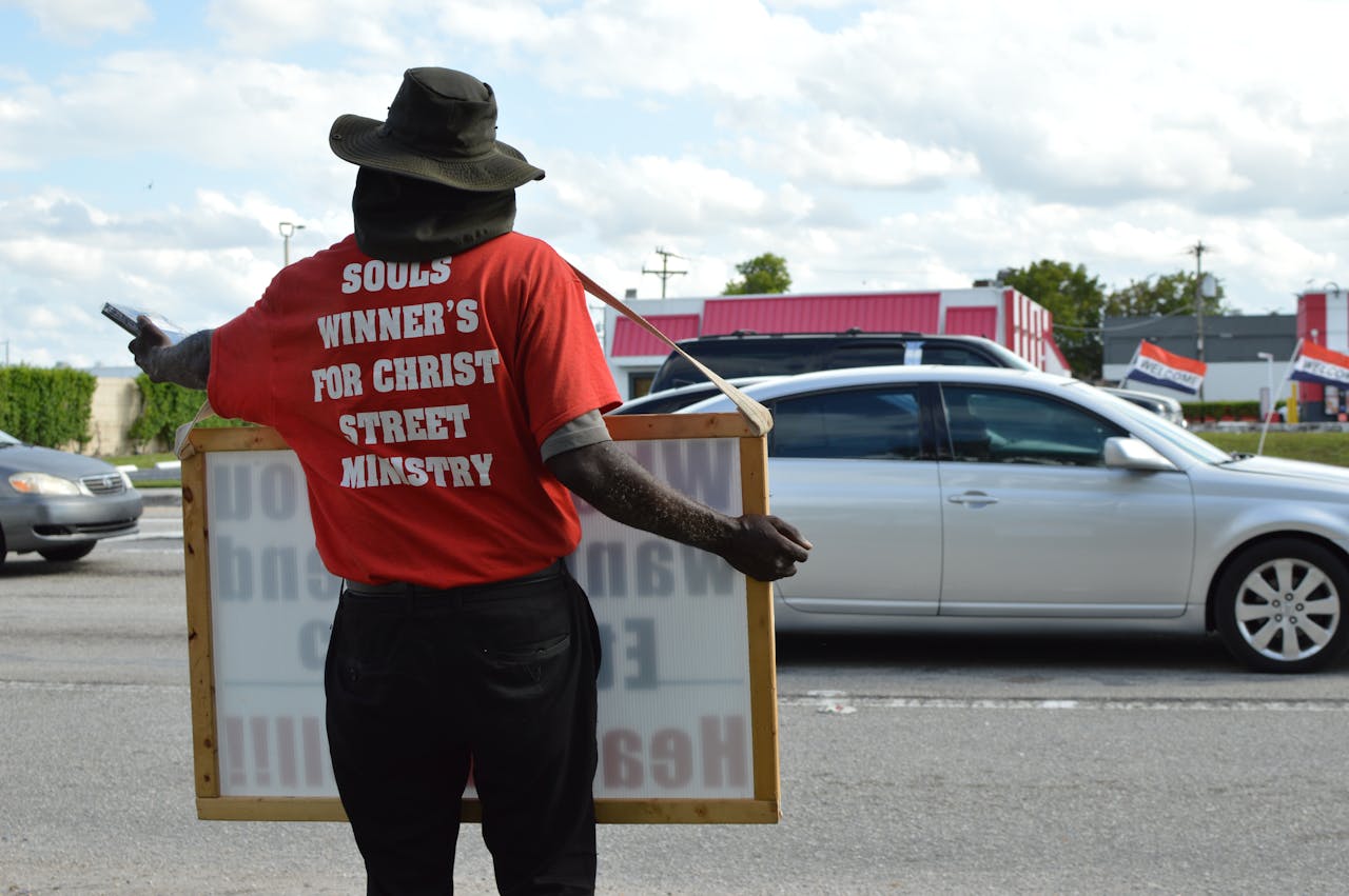 Individual holding ministry sign on busy street showcasing religious message
